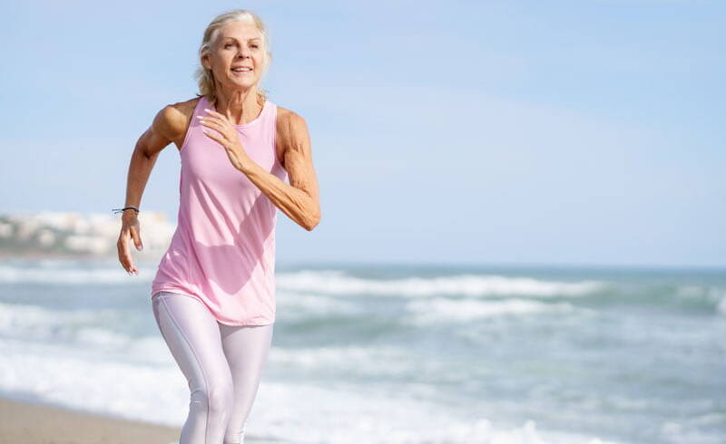 Mature woman running along the shore of the beach, signifying the positive impact of Sentral IVs on lung health